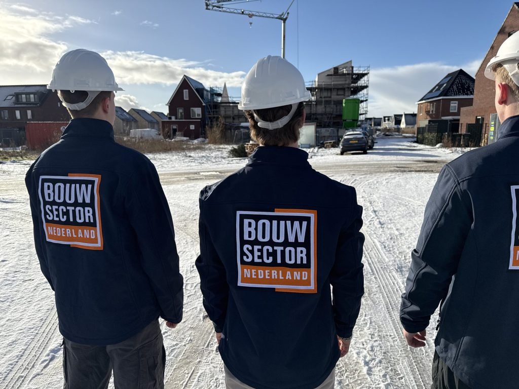 Drie vakmensen van Bouwsector Nederland met witte helm voor een rij huizen in aanbouw